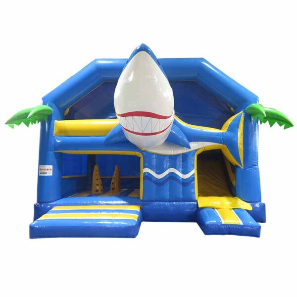 Un Château Combo gonflable Baby Shark bleu et jaune conçu comme un requin. L'entrée est un toboggan ressemblant à la gueule du requin, avec des palmiers décoratifs supplémentaires de chaque côté. L'intérieur présente des éléments d'escalade amusants et des motifs de vagues vibrants.