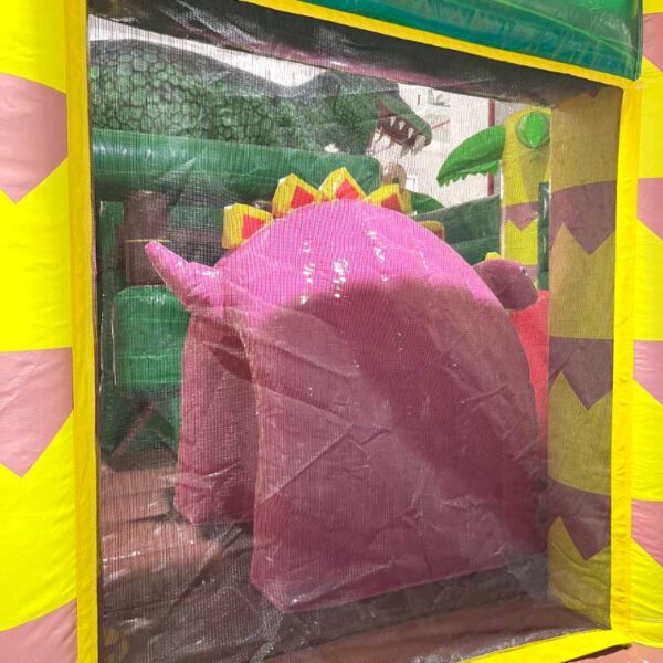 Une structure de jeu gonflable aux couleurs vives à l'intérieur d'un CHÂTEAU GONFLABLE DINO WORLD, mettant en vedette un grand dinosaure rose avec des pointes jaunes et un dinosaure vert avec des dents pointues en arrière-plan. La structure est bordée d'un cadre jaune et rose, et recouverte d'une enceinte grillagée.