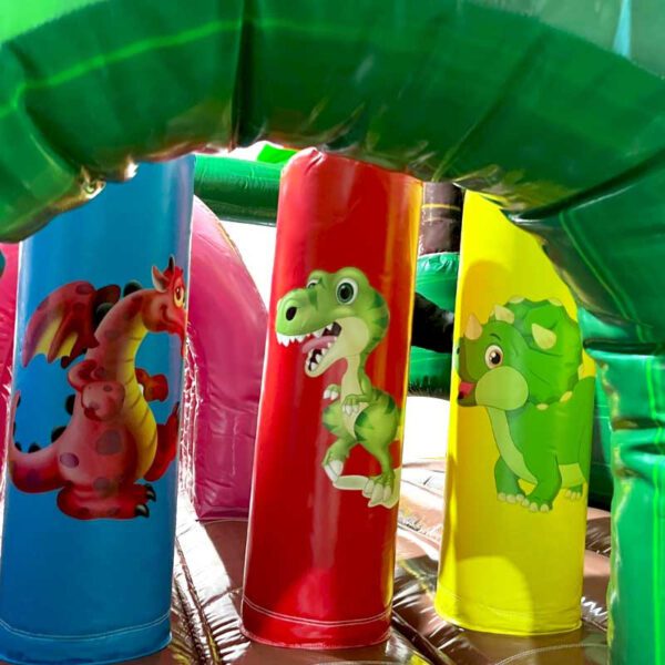Gros plan d’une structure de jeu gonflable colorée comportant trois piliers cylindriques. Chaque pilier est décoré d'un dinosaure de dessin animé : un dinosaure rouge ressemblant à un dragon, un T-Rex vert et un tricératops vert. L'arrière-plan comprend davantage d'éléments gonflables. Nom du produit : CHÂTEAU GONFLABLE DINO WORLD