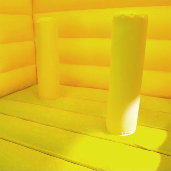 Vue intérieure d'un CHÂTEAU GONFLABLE WESTERN jaune vif. Le sol et les murs sont constitués d'un matériau gonflable jaune et deux piliers gonflables cylindriques se dressent au milieu. La chaude lumière du soleil illumine l’espace.