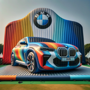 Une grande voiture gonflable BMW colorée est exposée devant un fond gonflable de conception similaire comportant le logo BMW en haut. La scène, parfaite pour un anniversaire d’enfant, se déroule en plein air pendant la journée avec des tentes visibles en arrière-plan.